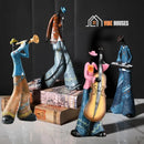 In the image four musicians: Keyboard-Ray. Cello-Ron. Trumpet-Miles.Singer-Louis is on two books. Vibe Houses