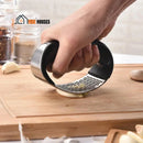 Premium stainless steel garlic press!; a hand is squeezing the garlic with the press on a wooden board; order now; vibe Houses