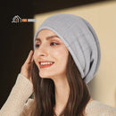 CozyMuse women's beanie. Woman smiling with her face slightly turned to the side. She has one hand over her ear. She is wearing a gray beanie. vibe houses