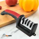 Scissor And knife Sharpener – On a table there is a wooden board with some fruit and next to it is the sharpener of knives and scissors. SharpMaster by Vibe Houses.