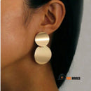 Earrings – Golden Double Disc; a woman has her face turned away, she has long black hair and is wearing an earrings; vibe houses