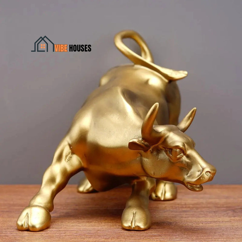 Wall Street Bull Statue - Golden; This one facing front ; On a wooden table all the beauty of the statue stands out; vibe houses; 